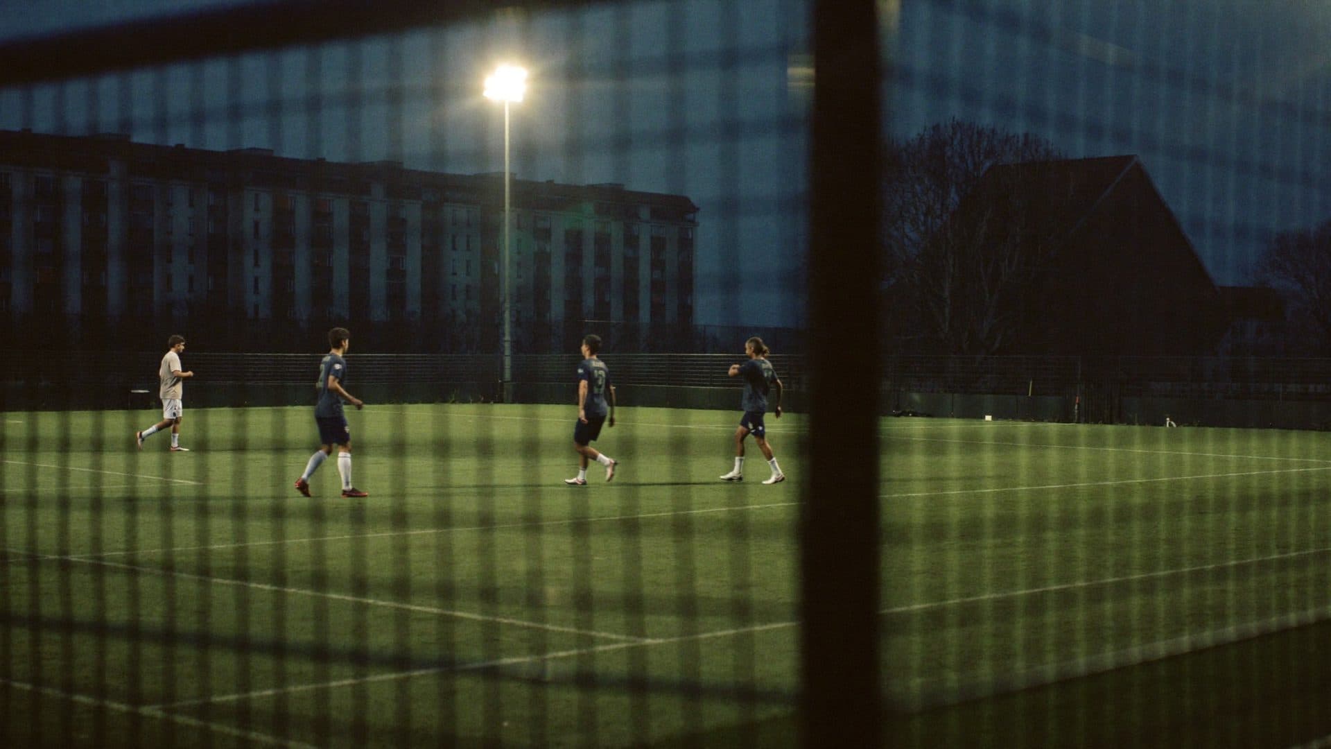 A five a side pitch under floodlights on a cold evening, seen through the fence