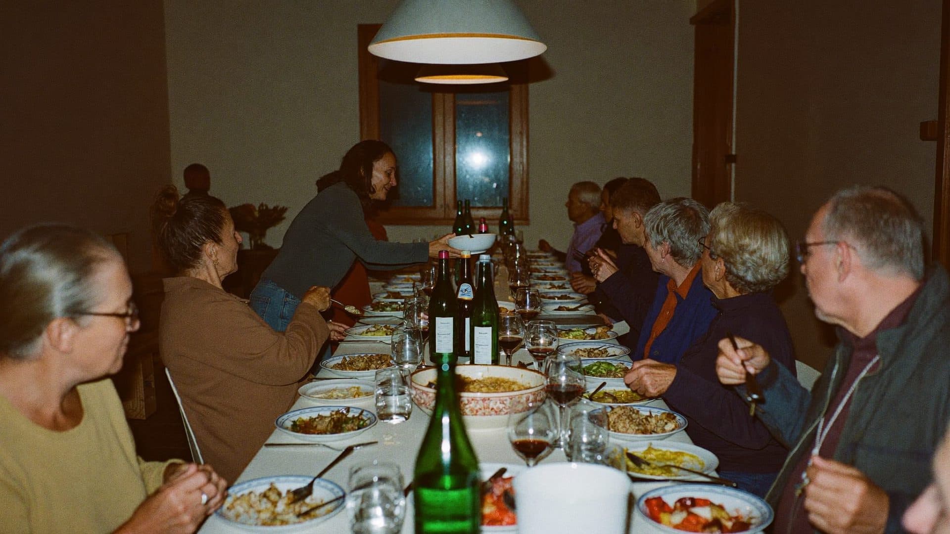 A long table laid for dinner, with dishes being passed under low pendant lights